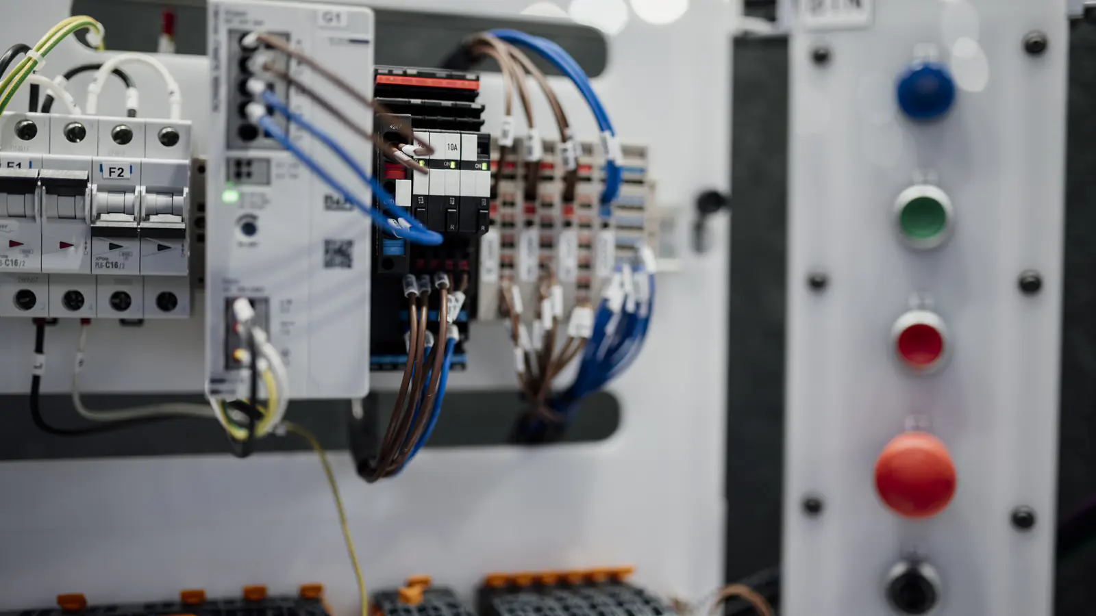 Wiring, circuit breakers and terminal blocks in a control panel beside coloured push buttons.