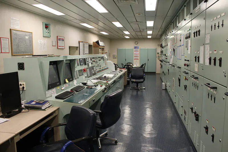 Ship engine control room with a control console and switchboard panels.