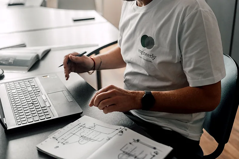 Engineer reviewing a document beside a laptop.